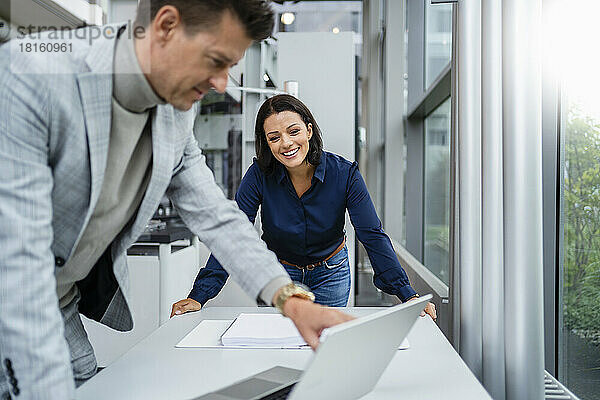 Glücklicher Geschäftsmann zeigt glücklicher Geschäftsfrau am Schreibtisch Laptop