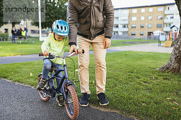 Vater bringt Sohn bei  auf der Straße Fahrrad zu fahren