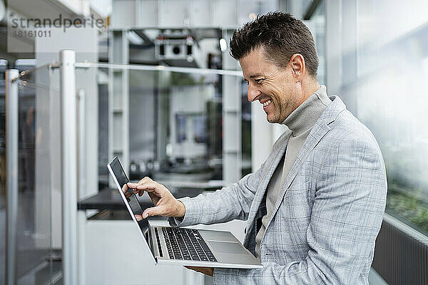 Glücklicher Geschäftsmann berührt Laptop-Bildschirm in der Industrie