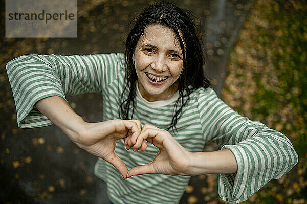 Glückliche Frau gestikuliert Herz mit Händen im Park
