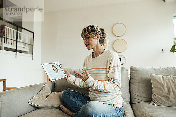 Schwangere Frau diskutiert mit Arzt über Tablet-PC  sitzt zu Hause auf dem Sofa