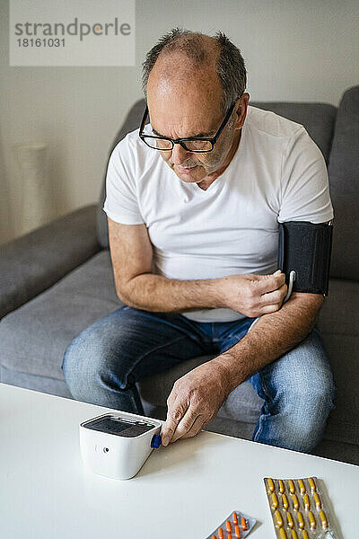 Älterer Mann überprüft den Blutdruck mit einem Gerät im Wohnzimmer