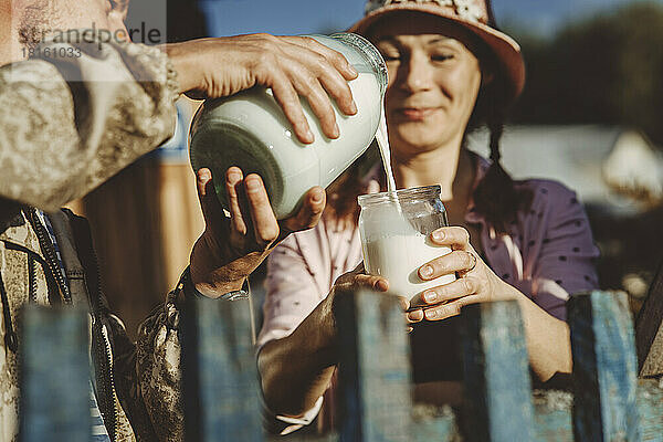 Mann gießt an einem sonnigen Tag Milch in das Glas seiner Freundin