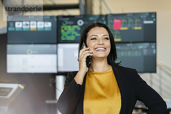 Glückliche Geschäftsfrau  die vor Computermonitoren mit dem Mobiltelefon spricht