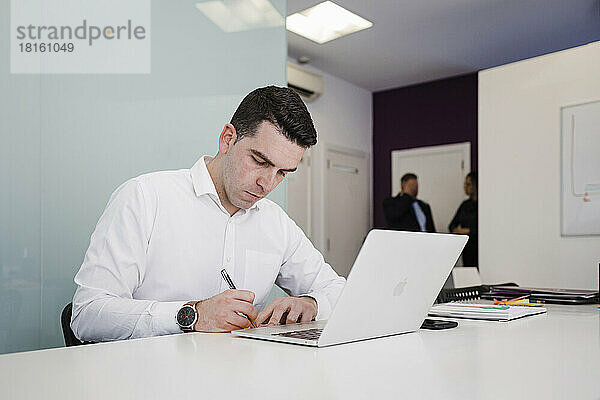 Junger Geschäftsmann schreibt vor Laptop am Schreibtisch im Büro