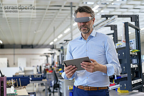 Reifer Geschäftsmann trägt einen Virtual-Reality-Simulator und hält einen Tablet-PC in der Industrie
