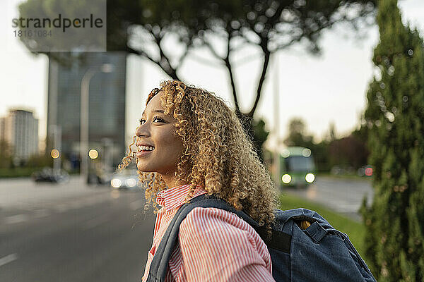 Lächelnde blonde Frau mit Rucksack  die über den Sonnenuntergang nachdenkt