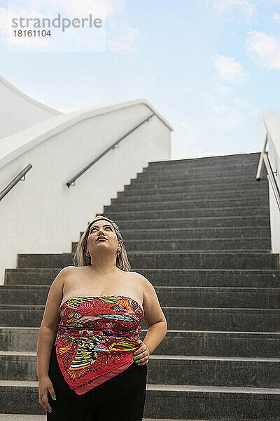 Frau steht mit der Hand auf der Hüfte vor der Treppe