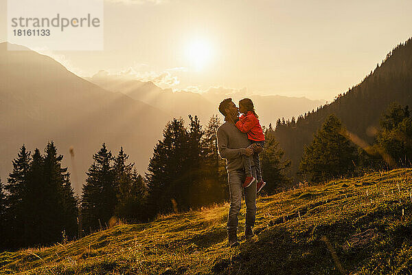 Vater küsst Tochter bei Sonnenuntergang auf dem Berg