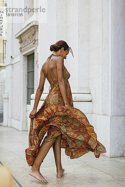 Junge Frau im Sommerkleid läuft vor dem Gebäude