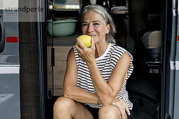 Frau isst Apfel am Eingang eines Wohnmobils