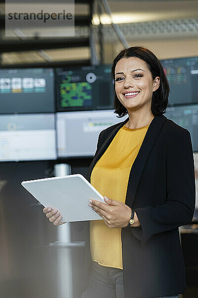 Lächelnde Geschäftsfrau hält Tablet-PC vor Computermonitoren