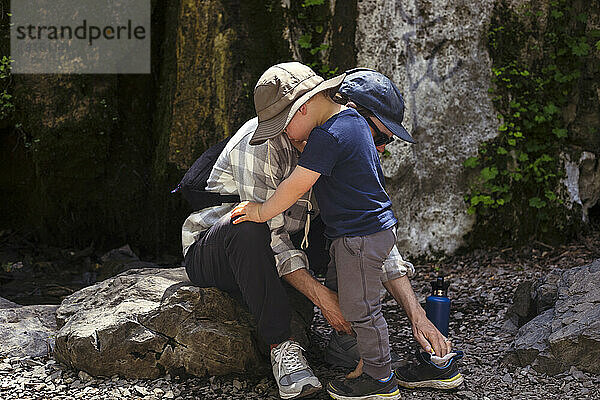 Vater hilft Sohn  Schuh auf Felsen zu tragen