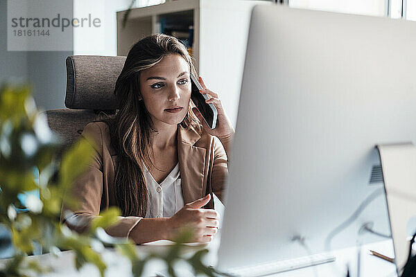 Junge Geschäftsfrau telefoniert vor dem Desktop-PC