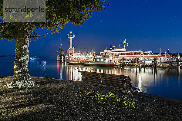Deutschland  Baden-Württemberg  Konstanz  Hafen am Bodenseeufer bei Nacht mit leerer Bank im Vordergrund