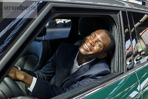 Cheerful businessman with eyes closed enjoying sunny day through car window