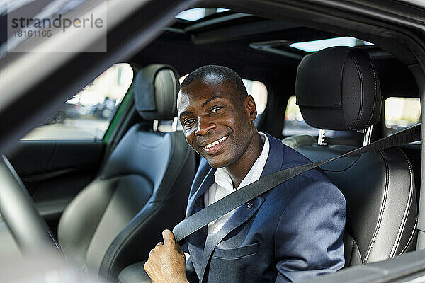 Happy businessman fastening seat belt in car