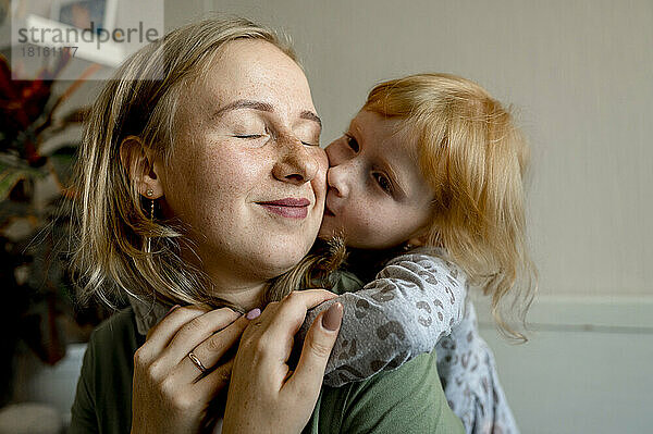 Daughter embracing mother from behind and kissing her on cheek at home