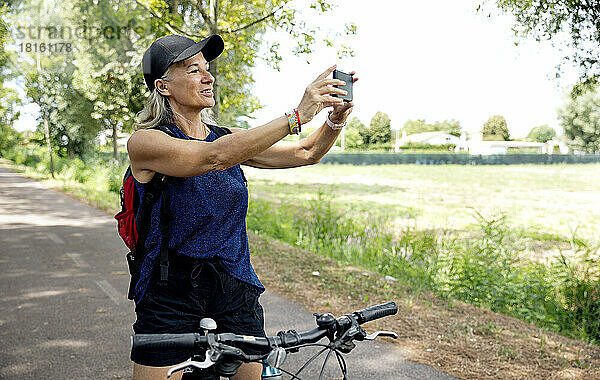 Lächelnde ältere Frau fotografiert mit dem Smartphone auf dem Fahrrad