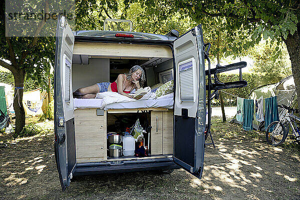 Ältere Frau liegt im Wohnmobil und liest Buch