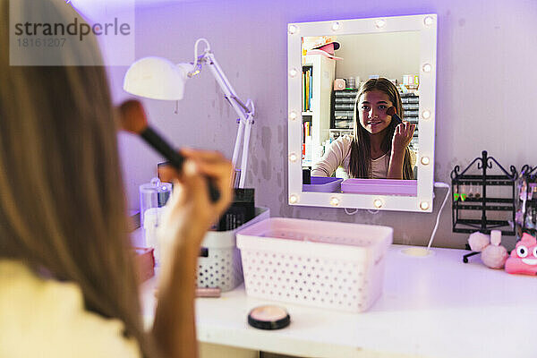 Mädchen trägt Make-up mit Pinsel auf und schaut zu Hause in den Spiegel