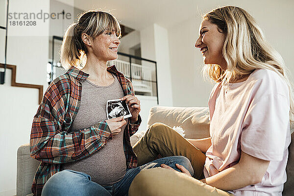 Lächelnde Schwester spricht mit schwangerer Frau  die zu Hause Ultraschall hält