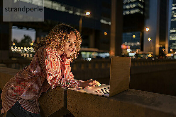 Lockige Frau mit der Hand am Kinn und Laptop in der Stadt