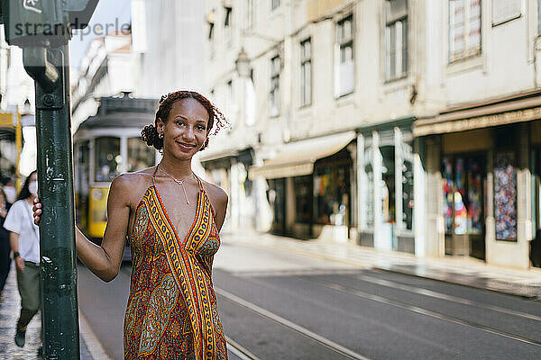 Lächelnde junge Frau  die an der Stange auf dem Fußweg steht