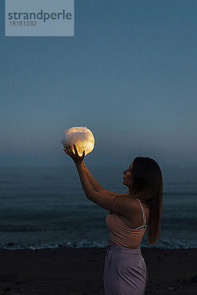 Junge Frau hält einen Stoffball mit Licht  das den Mond in der Nacht simuliert
