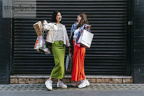 Happy lesbian women with shopping bags standing in front of shutter