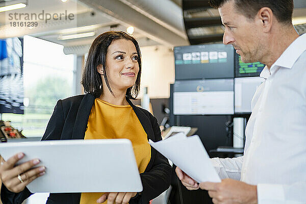 Lächelnde Geschäftsfrau mit Tablet-PC und Blick auf Kollegen in der Industrie