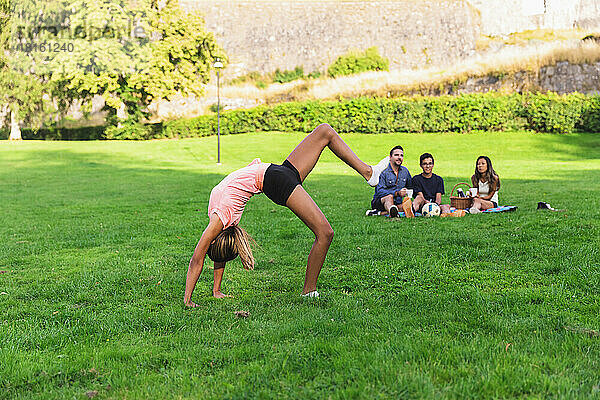 Mädchen macht Akrobatik  während die Familie im Hintergrund beim Picknick sitzt