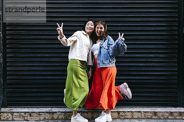 Cheerful lesbian couple showing peace sign in front of shutter