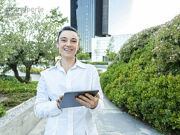 Glückliche Geschäftsfrau mit Tablet-PC steht am Fußweg