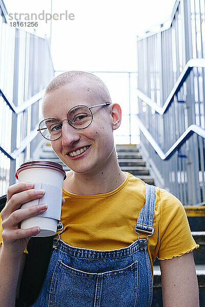 Lächelnde nicht-binäre Person mit Einwegkaffeetasse und Brille