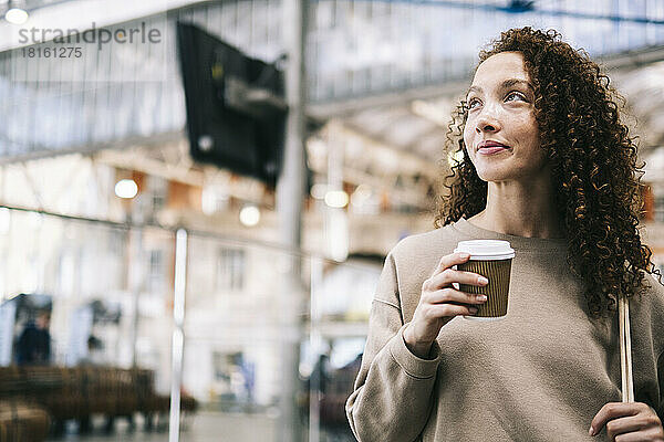 Lächelnde Frau mit Einwegbecher Kaffee am Bahnhof