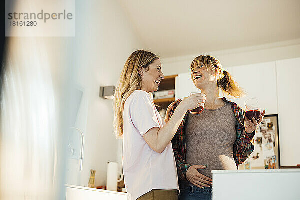 Happy pregnant woman enjoying drink with sister at home