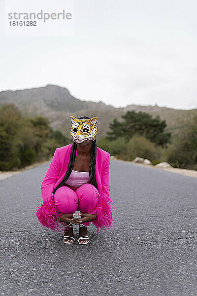 Junge Frau mit Tigermaske kauert auf der Straße