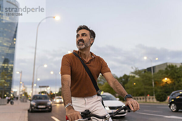 Reifer Geschäftsmann mit Fahrrad steht bei Sonnenuntergang am Straßenrand in der Stadt