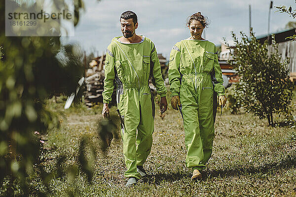 Happy beekeepers wearing protective suits walking together on apiary