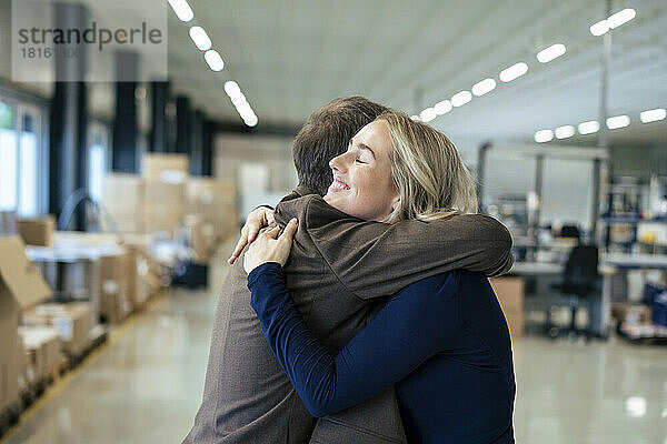 Lächelnde Geschäftsfrau umarmt Kollegen in der Industrie