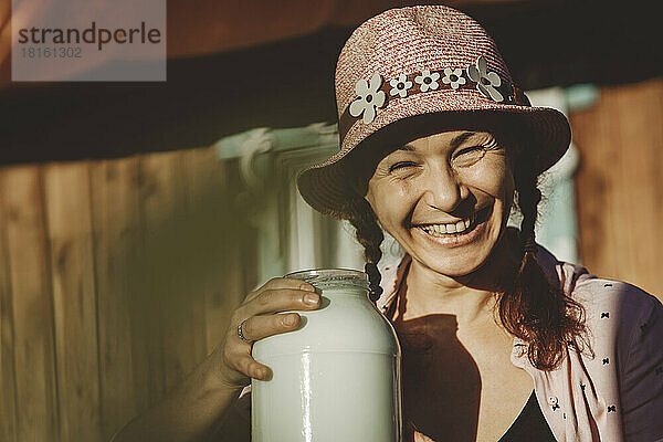 Fröhliche Frau mit Eimerhut und Glas Milch an einem sonnigen Tag