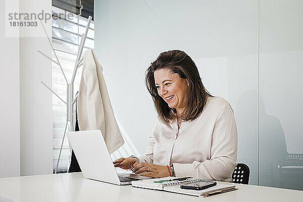 Glückliche Geschäftsfrau  die am Schreibtisch im Büro am Laptop arbeitet