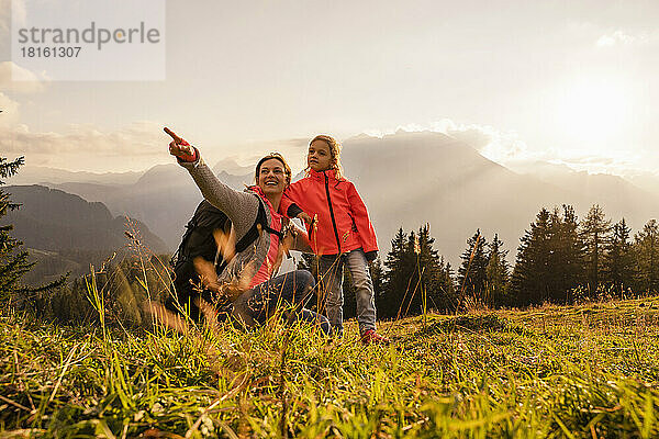 Lächelnde Frau zeigt auf ihre Tochter  die auf dem Berg steht