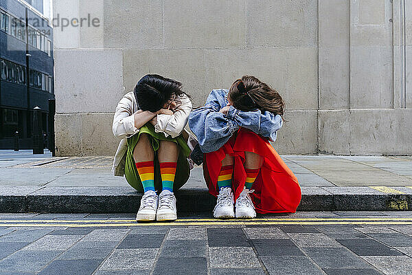 Junges lesbisches Paar mit auf Armen ruhendem Kopf sitzt zusammen am Fußweg