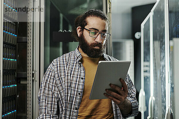 Techniker mit Brille blickt im Serverraum auf Tablet-PC