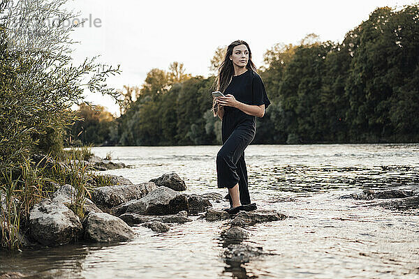 Junge Frau mit Mobiltelefon steht im See