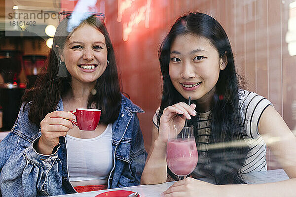 Glückliches lesbisches Paar beim Drink im Café  gesehen durch das Fenster