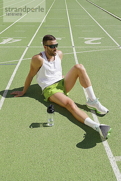 Müder Sportler mit Sonnenbrille entspannt sich auf der Sportstrecke
