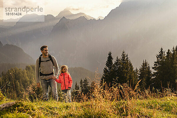 Lächelnder Mann hält die Hand seiner Tochter beim Wandern auf dem Berg